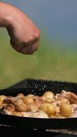 Frying pan from disc harrow with a lid for cooking over an open fire. The cook's hand salts the roasting new potatoes close-up. video