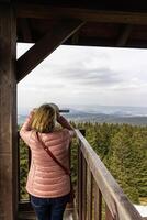 Woman looking through a telescope at a mountain landscape. Eastern Sudetes on the border of Poland and the Czech Republic photo