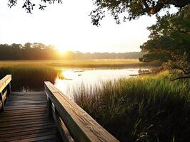 Serene landscape at sunset over a marsh, featuring a wooden boardwalk and lush greenery in the foreground. photo