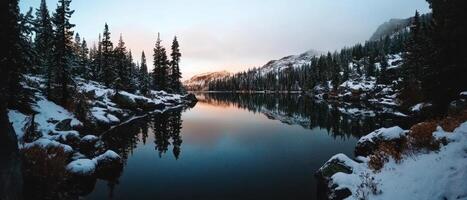 Serene winter landscape featuring a calm lake surrounded by snow-covered trees and mountains under a soft, pastel sky. photo