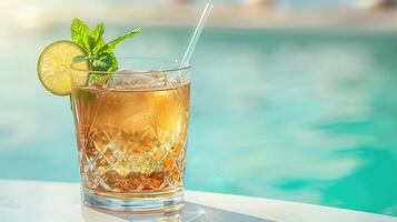 tropical alcoholic cocktail in a glass with ice cubes, a lime wedge and a mint leaf on the edge of a swimming pool at a summer resort photo