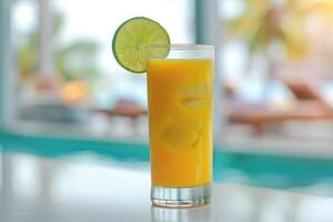 tropical mango cocktail with ice in glass with lime wedge on rim on sleek white bar counter at pool bar photo