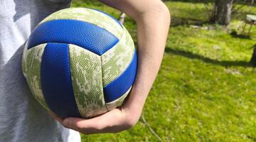 close up of volleyball in hands of girl playing volleyball on green meadow outdoors. Summer activity, team play photo