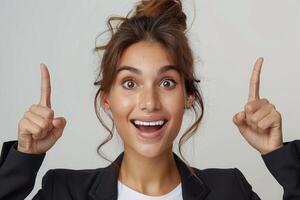 Surprised Smiling young woman in business suit pointing up with both hands. Confident and friendly expression. Suitable for advertising and promotion. photo