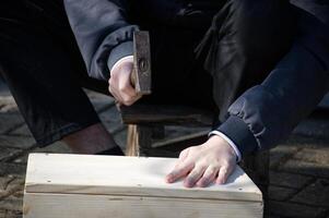 A man hammers nails into a simple wooden box he's constructing outside in the bright sunlight. photo