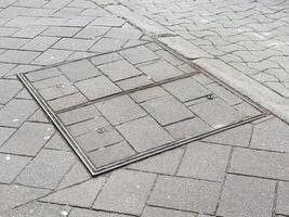 Rectangular metal manhole cover on brick pavement and asphalt road photo
