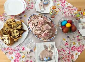 Easter brunch table with sliced meat, pastries, and colored eggs on floral tablecloth photo