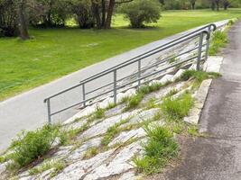 Park path with metal railing and overgrown grass in spring photo