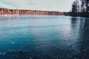 frozen lake with snowflakes in the foreground, surrounded by a wintry forest photo