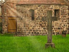 A historic stone cross in front of an old rustic church with small windows. photo