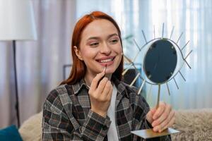 Young pretty woman applying makeup looking in mirror smiling while drawing lips with lipstick gently photo