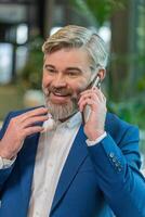Mature businessman in formal suit answering to client on mobile phone call in modern office lobby photo