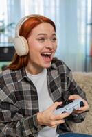 Young woman on sofa playing game with joystick emotionally reacting to action on screen photo