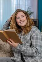 Woman sitting on sofa opening and reading book with focus thoughtfully flipping pages and reflecting photo