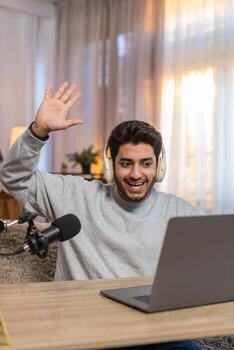 Hindu man using laptop recording vlog and conducting online stream while sitting at table at home photo
