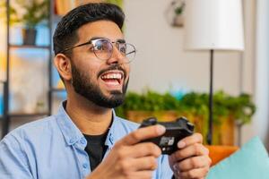Indian young man using joystick controller playing console game online game on home sofa photo