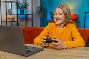 Teenager boy playing football sports simulator on laptop with joystick, celebrating goal at home photo