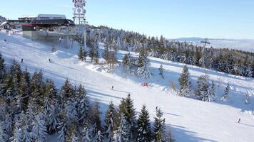 Aerial view of snowy ski resort with people skiing down the slope on a sunny day video