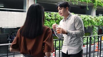 Asian office employee holding drink talking with colleague while taking a break at the workplace talking with colleague video