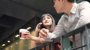 Asian woman talking on the phone standing with colleague while taking a break in the city while taking a break video