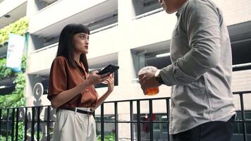 Asian office employee in casual style holding drink talking with colleague while taking a break at the workplace talking with colleague video