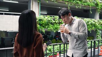 Asian office employee in casual style holding drink talking with colleague while taking a break at the workplace with colleague video