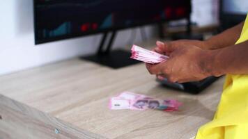 Hands Counting Currency Banknotes On Wooden Surface Near Computer Screen Displaying Charts video