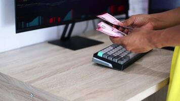 Hands Counting Currency at Desk with Market Data on Screen video