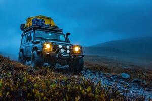 A rugged off-road vehicle equipped for adventure navigates a muddy path in a misty mountain landscape during rain at twilight, showcasing resilience in challenging weather conditions. photo