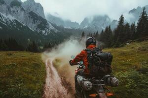 A motorcyclist navigates a rugged dirt path through lush greenery and mountainous terrain. Mist blankets the mountains, creating a serene yet adventurous atmosphere early in the day. photo