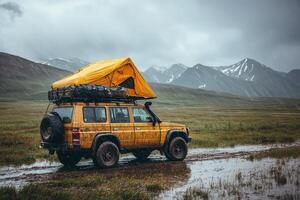 A yellow off-road vehicle with a rooftop tent is parked on a muddy path surrounded by towering mountains. Dark clouds suggest rain is imminent, adding to the adventures wild atmosphere. photo