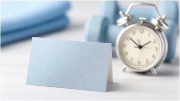 Blue Card on Table with Alarm Clock and Dumbbell Set in a Wellness or Fitness Concept Setting photo
