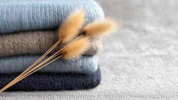 Soft Textures of Cozy Wool Sweaters Stacked with Decorative Dried Grasses on a Neutral Background photo