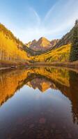 Tranquil Reflection of Majestic Mountains in Serene Lake Surrounded by Lush Autumn Foliage Under Clear Blue Sky photo