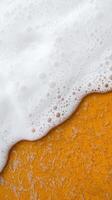 Aerial View of Soft Waves Gently Touching a Vibrant Orange Beach with Texture and Bubbles photo
