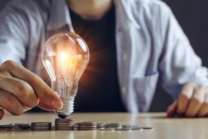New idea concept with coins stack save power to save the earth, young Asian Men hand holding light bulb with new knowledge light bulb and money stack on wood table and on black background. photo