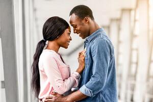 Portrait Of Romantic Black Couple Hugging In Airport Terminal While Waiting For Flight Boarding, Happy African American Newlyweds Ready For Honeymoon Vacation Trip, Embracing And Smiling, Side View photo