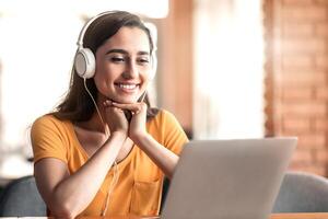 Smiling arab girl having call while resting at cafe, using laptop and headset, empty space photo