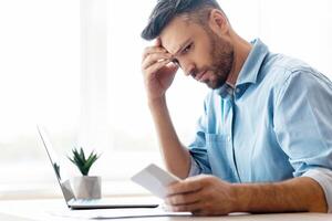 Concerned young businessman looking at smartphone working in office, waiting message, received bad sms with threat, using cellphone, touching forehead with thoughtful face expression, copy space photo
