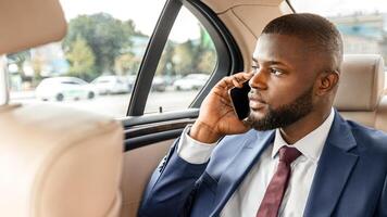 Black manager sitting on back seat in car and using digital tablet, checking email, having phone call, copy space. Handsome african american businessman going to meeting, working on a way to office photo
