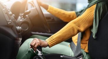 Unrecognizable Black Muslim Lady In Hijab Driving Car, Holding Gear Shift Knob, Smiling African Islamic Woman Enjoying Ride In Her New Vehicle, Selective Focus On Transmission Handle, Cropped Image photo