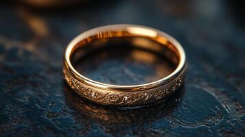 A beautifully crafted gold wedding band with detailed engravings is set on a rustic black surface, illuminated by soft, warm light, evoking a sense of love and commitment. photo