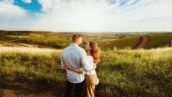 Caring Relationship. Back view of man and woman in love standing in the field, embracing and looking at each other photo