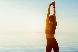 Wellbeing Concept. Rear view of slim lady stretching her arms and looking at the sea and sunrise, free space photo