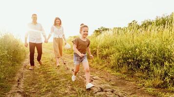 Happy Childhood Concept. Little girl running on the road, mom and dad walking in the background holding hands photo