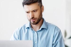 Concentrated businessman working on laptop at workplace in office, male entrepreneur looking at computer screen and typing on keyboard, filling report, answering emails, managing project, copy space photo