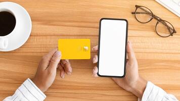 Easy Pay. Above view of woman using credit card and blank smart phone with white mock up, wooden table background photo