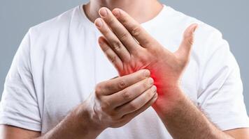 Dermatitis, eczema, allergy, psoriasis concept. Unrecognizable man scratching itch on his hand, grey studio background. Closeup of man itching rash on his hand, sore zone highlighted with red, cropped photo