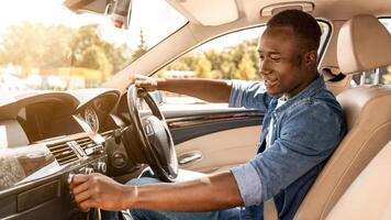 Excited young black man in casual sitting in comfy automobile, turning on music on dashboard before moving to office or beginning car trip, enjoying his new auto, side view, copy space photo
