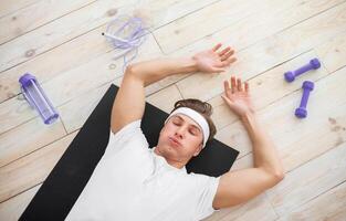 Weight loss from effective workout. Tired athlete with dumbbells and rope lying on mat on floor and takes breath at home, top view, free space photo